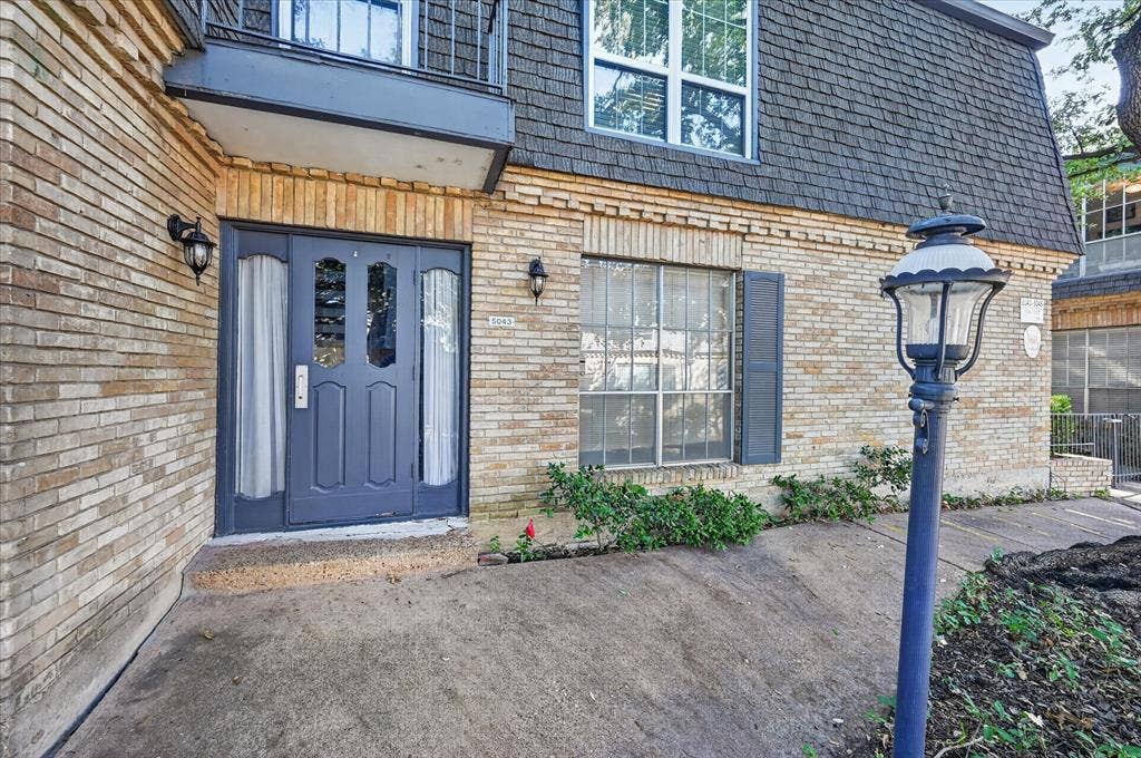 5043 Les Chateaux Drive, #214, Dallas, TX 75235 Condo entry through the parking area. Brick exterior with a dark-paneled entry door, adjacent sidelights, and exterior wall sconces
