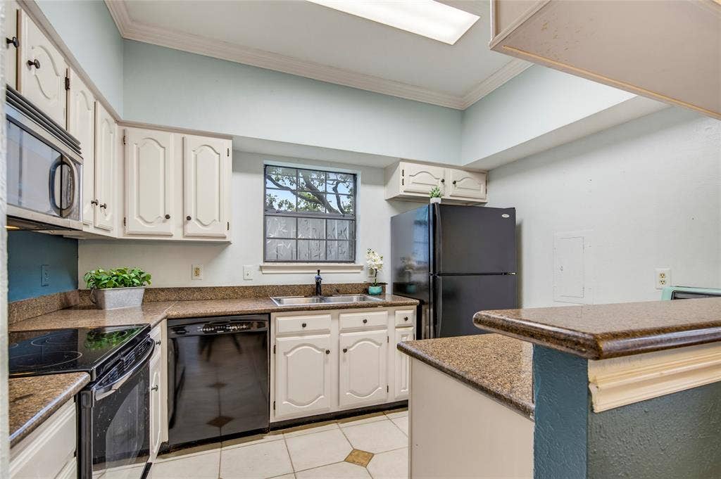 The cutest kitchen featuring beige cabinetry, granite countertops, black appliances, and tile flooring with accent colors....the fridge comes with the condo....