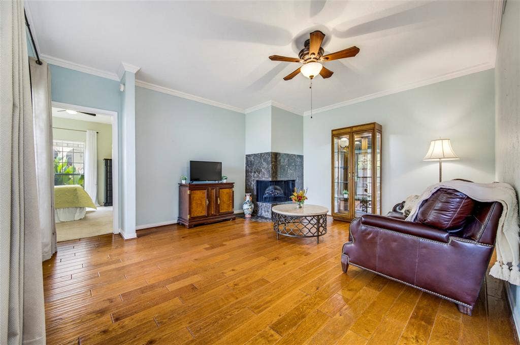 Engineered hardwood flooring, crown molding, ceiling fan with integrated lighting, and a beautiful corner fireplace