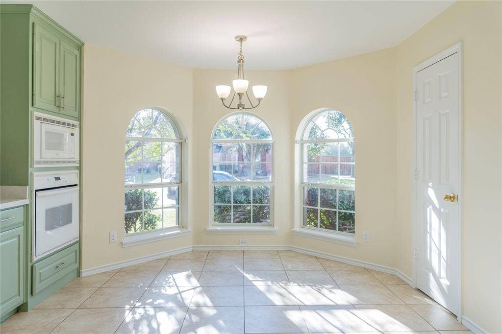15534 Durango Drive, Frisco, TX 75035 Built-in white microwave and oven, green cabinetry, three arched windows, ceiling-mounted chandelier, and tile flooring