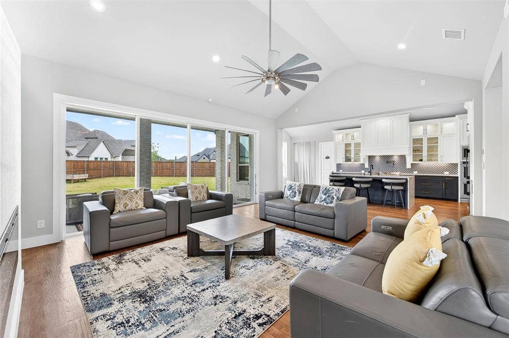 3312 Crosby Lane, Celina, TX 75009 Vaulted ceilings with recessed lighting, wood-finish flooring, expansive sliding glass doors, contemporary ceiling fan, and a kitchen with white and dark cabinetry