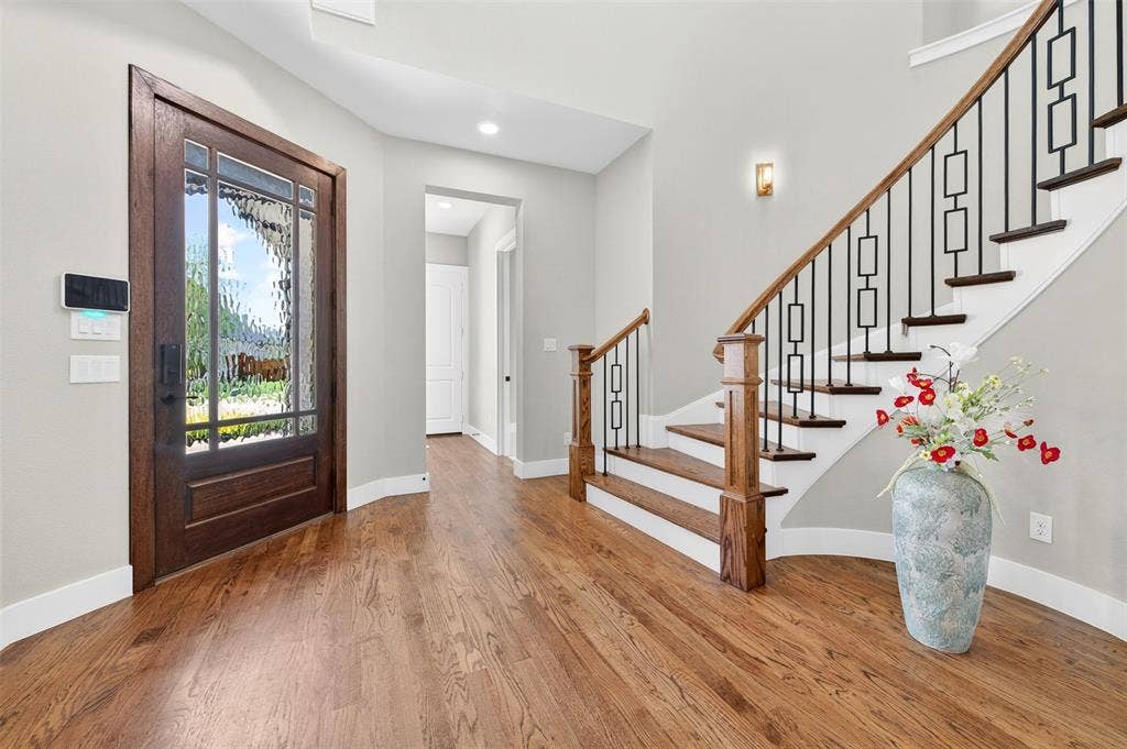 3312 Crosby Lane, Celina, TX 75009 Hardwood flooring, wood staircase with iron balusters, recessed lighting, stained wood entry door with textured glass, and a wall sconce