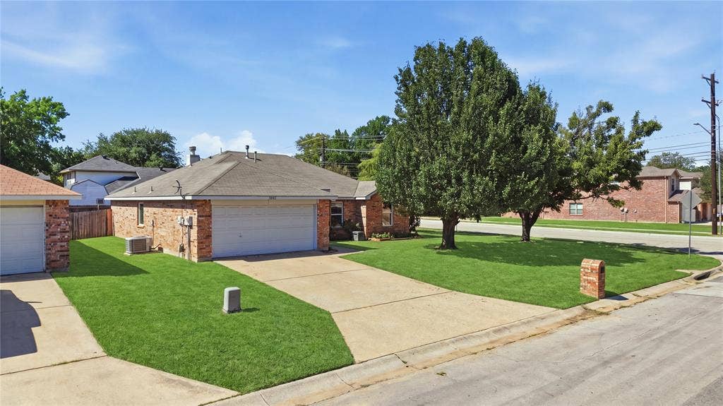 1125 Bayfield Drive, Denton, TX 76209 Brick exterior with a gabled roofline, front-facing garage, concrete driveway, and mature landscaping