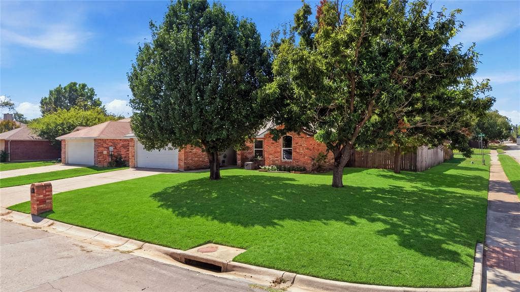 1125 Bayfield Drive, Denton, TX 76209 Brick exterior with an attached two-car garage, mature front yard trees, and a concrete driveway
