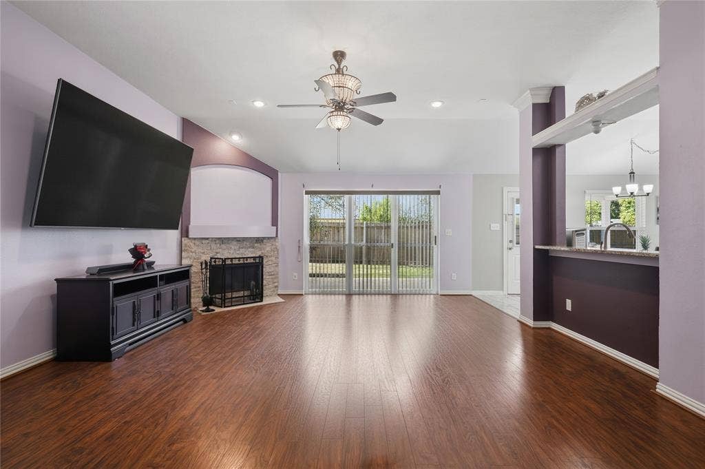 1125 Bayfield Drive, Denton, TX 76209 Spacious living area featuring wood-finish flooring, a stone-faced fireplace with hearth, and a ceiling fan with integrated lighting