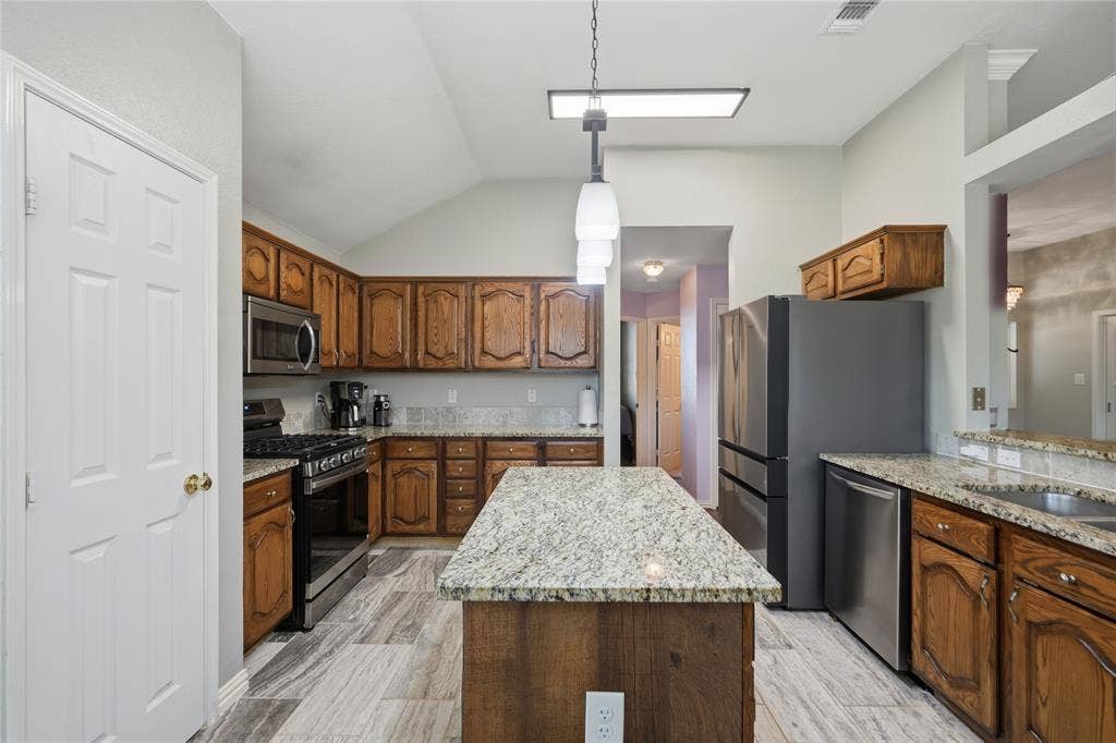 1125 Bayfield Drive, Denton, TX 76209 Kitchen featuring wood cabinetry, light-toned granite countertops, stainless steel appliances, and wood-finish flooring