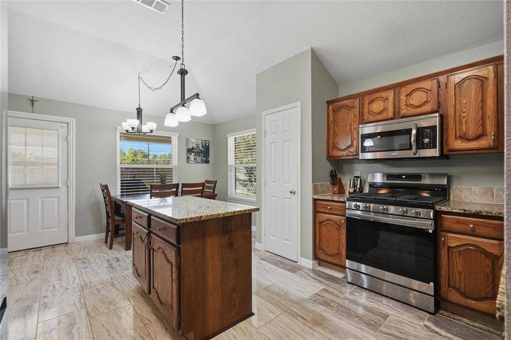 1125 Bayfield Drive, Denton, TX 76209 Kitchen featuring wood-finish cabinetry, stainless steel appliances, granite countertops, and wood-look tile flooring