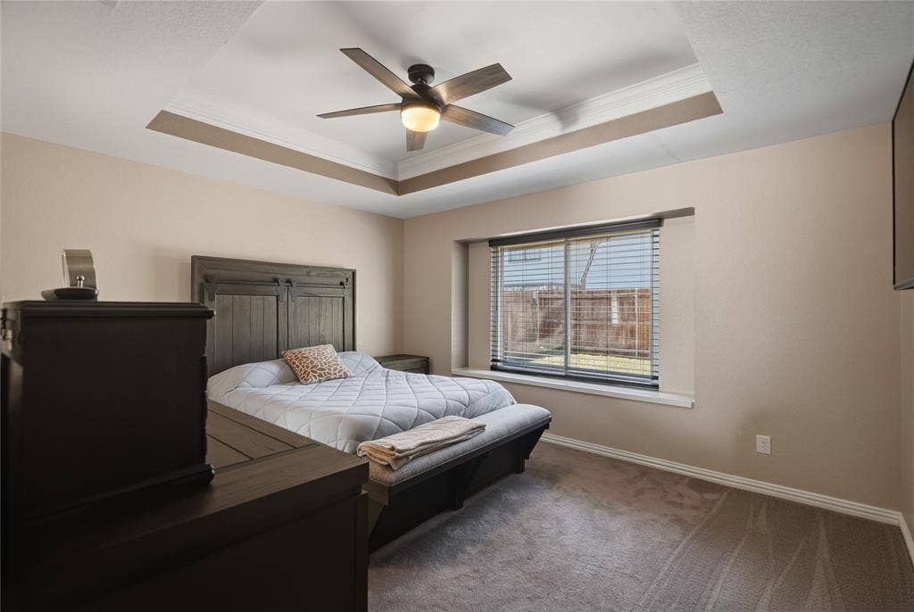 1125 Bayfield Drive, Denton, TX 76209 Recessed tray ceiling with crown molding, ceiling fan with integrated lighting, window with blinds, and carpeted flooring