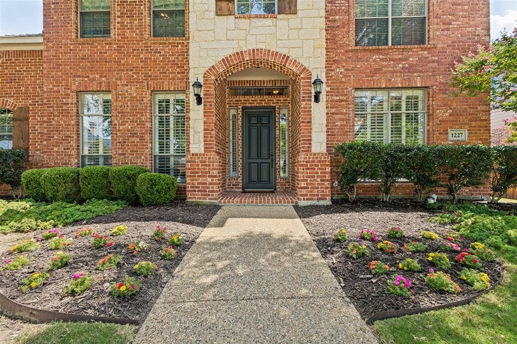 1227 Comanche Drive, Allen, TX 75013 Brick and stone facade featuring an arched entryway with sconce lighting
