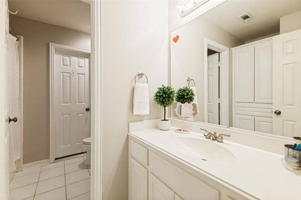 1227 Comanche Drive, Allen, TX 75013 Bathroom vanity featuring a white countertop with integrated sink, brushed nickel faucet, and a large wall-mounted mirror