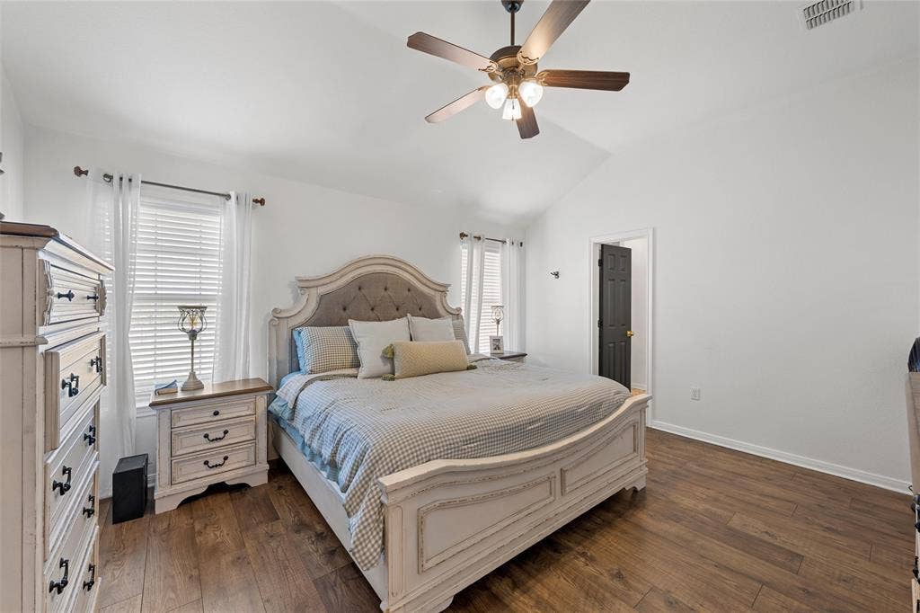 Vaulted ceiling with a ceiling fan, wood-finish flooring, white walls, and a dark paneled door