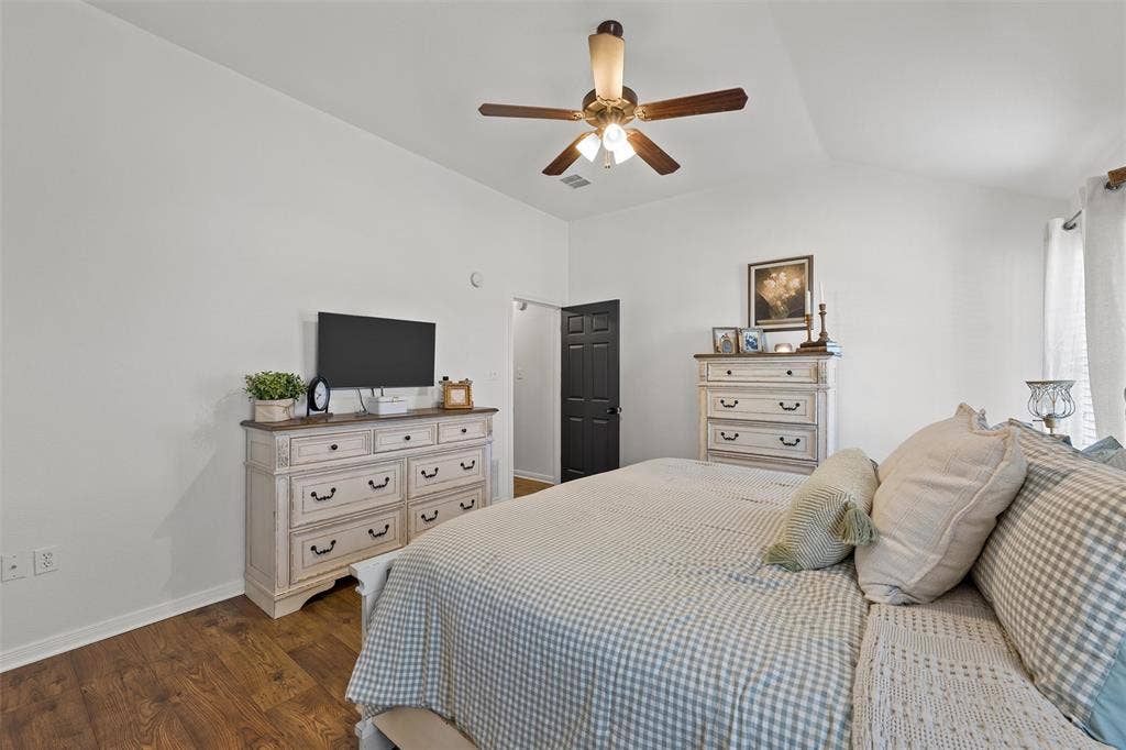 Vaulted ceiling, wood-finish flooring, ceiling fan with integrated lighting, and a dark paneled interior door