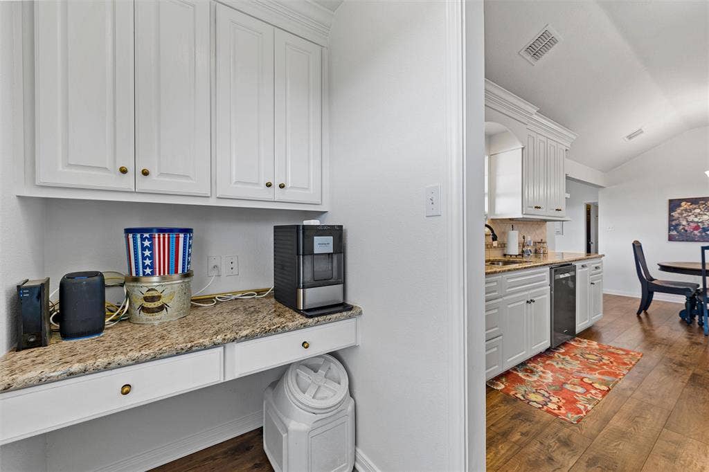 White cabinetry with brass hardware, speckled countertop, wood-finish flooring, and vaulted ceiling