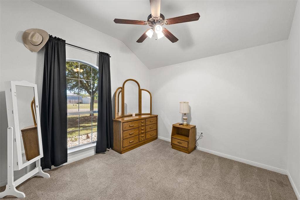 Vaulted ceiling featuring a ceiling fan with integrated lighting, arched window, and carpeted flooring