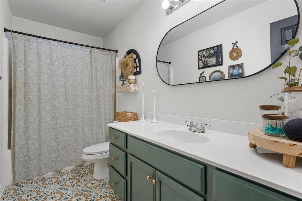 Custom tile flooring, a sleek vanity with a solid surface countertop, an oval-shaped mirror, and a built-in toilet