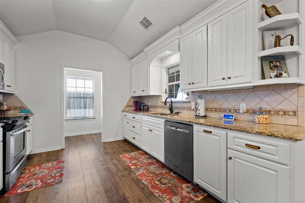 Kitchen featuring white cabinetry, granite countertops, tile backsplash, wood-finish flooring, and vaulted ceiling