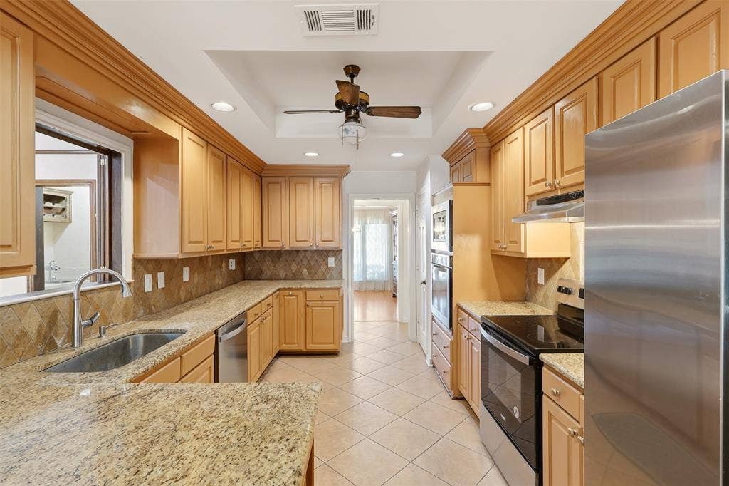 2700 Nighthawk Drive, Plano, TX 75025 Gourmet kitchen featuring extensive cabinetry, granite countertops, stainless steel appliances, and a tray ceiling with a ceiling fan