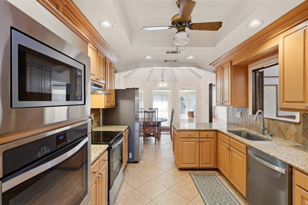 2700 Nighthawk Drive, Plano, TX 75025 Galley kitchen featuring wood cabinetry, stainless steel appliances, granite countertops, and tile flooring