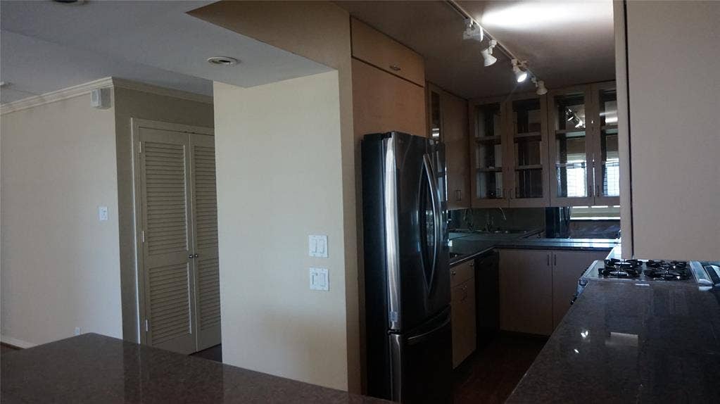 3883 Turtle Creek Boulevard, #1114, Dallas, TX 75219 Kitchen featuring a stainless steel refrigerator, dark stone countertops, wood-finish cabinetry with glass inserts, and a built-in cooktop