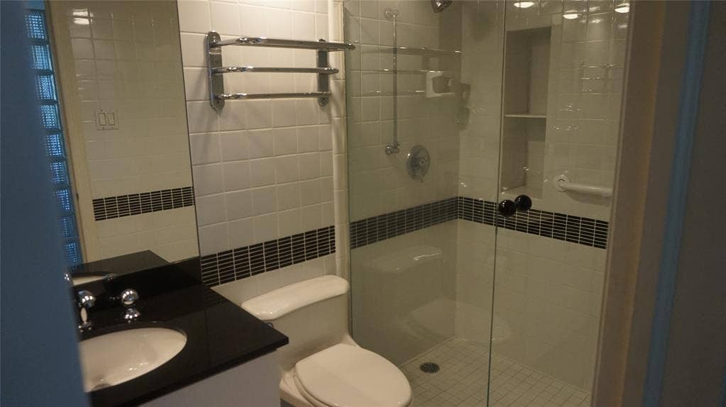 3883 Turtle Creek Boulevard, #1114, Dallas, TX 75219 Bathroom featuring a glass-enclosed shower, built-in shower shelving, a dark countertop vanity with an integrated sink, and white subway tile with a decorative accent band