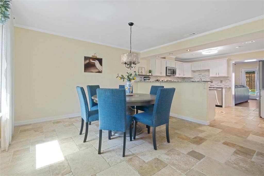 Open-concept dining area with large-format tile flooring, crown molding, and a decorative chandelier