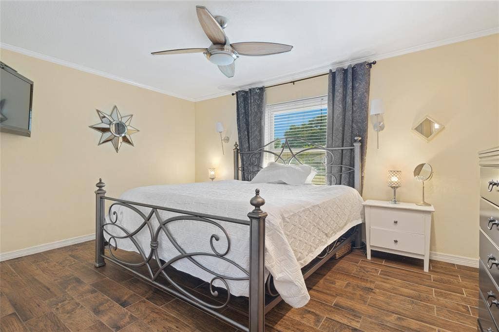 Wood-finish flooring, ceiling fan, crown molding, wall-mounted light fixtures, and window with blinds