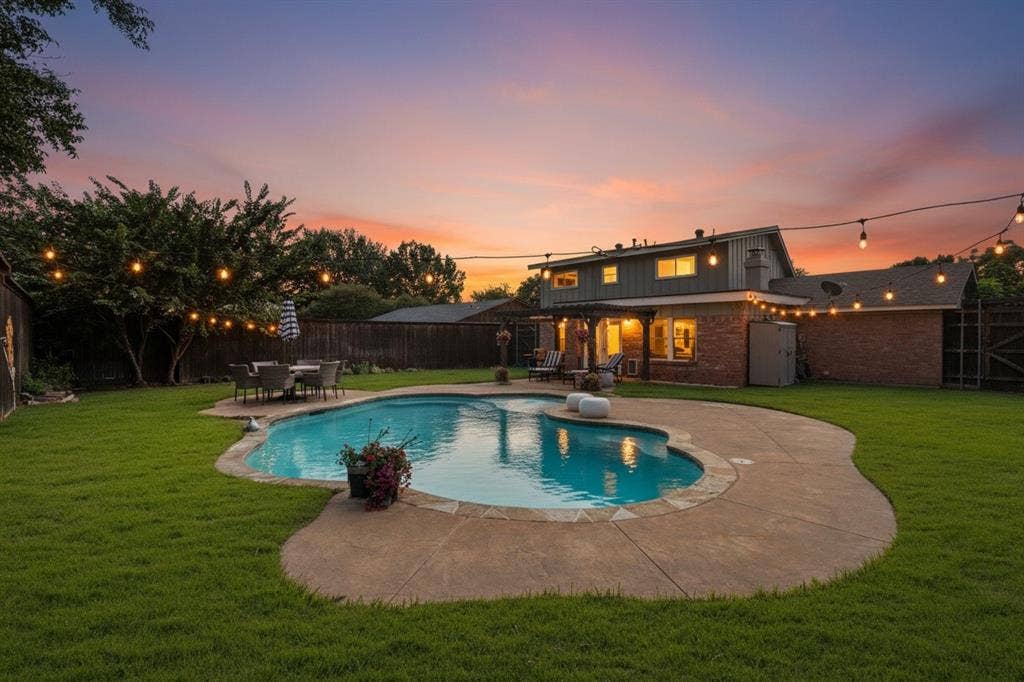 Manicured backyard featuring a freeform swimming pool with concrete decking