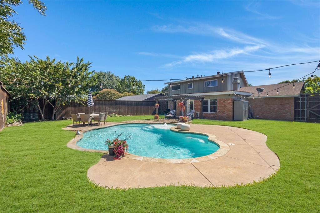 Expansive backyard featuring a custom-shaped swimming pool, surrounding concrete patio, and a privacy fence