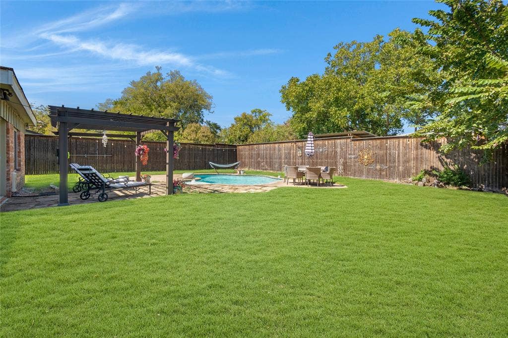 Expansive grass lawn with a swimming pool, stone paver patio, wood pergola, and wood privacy fencing