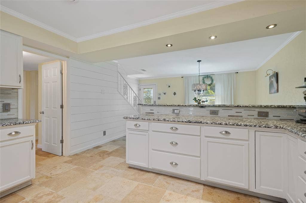 White cabinetry with polished hardware, granite-style countertops, mosaic tile backsplash, recessed lighting, and large format floor tiles