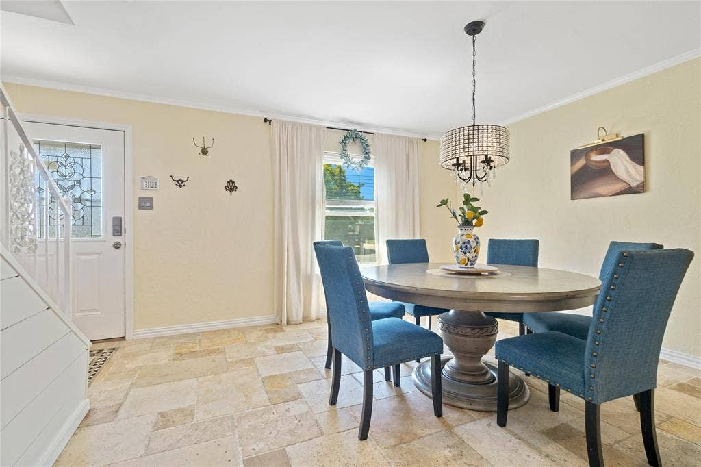 Travertine-style tile flooring, decorative leaded glass entry door, window with white drapery, and a chandelier with crystal-style accents