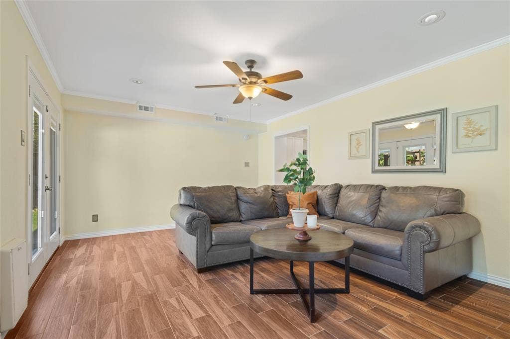 Wood-finish flooring, ceiling fan with integrated lighting, recessed lighting, crown molding, and double glass-paneled doors