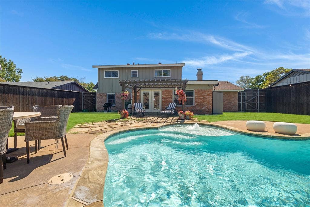 Curved swimming pool with stone coping, concrete patio, and a backyard pergola