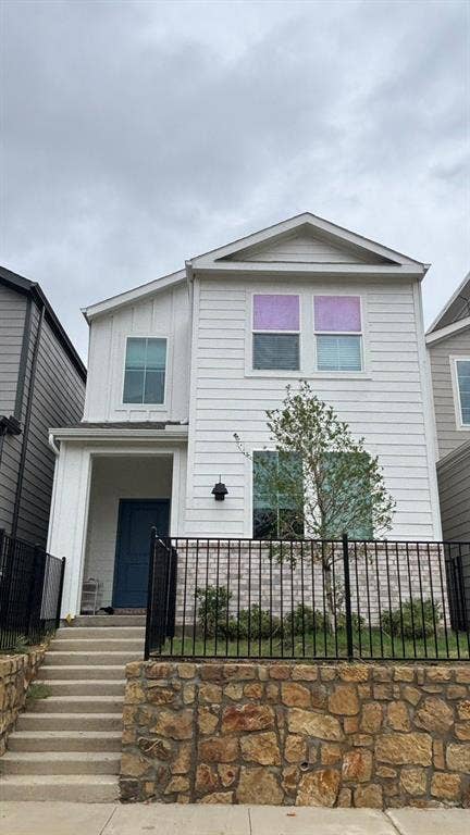 3308 Blue Jay Way, Richland Hills, TX 76118 Modern white siding exterior with a prominent blue entry door, featuring a stone retaining wall and black iron fencing