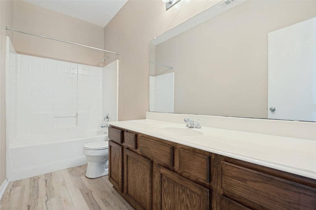 1308 Arbordale Court, Lancaster, TX 75134 Wood-finish flooring, dark wood cabinetry, white countertop with integrated sink, full-width vanity mirror, and a white tub with shower