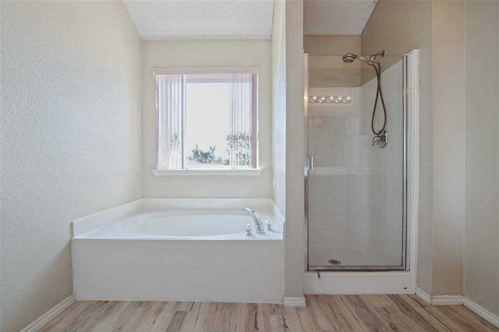 1308 Arbordale Court, Lancaster, TX 75134 Soaking tub with window, separate glass-enclosed shower, wood-finish flooring, and wall-mounted light fixture
