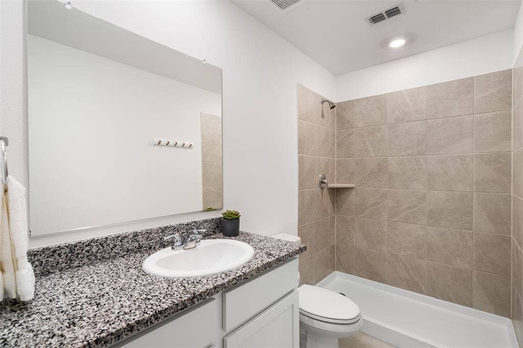 250 Herman Lane, Princeton, TX 75407 Granite-look countertop, undermount sink, large mirror, and tiled shower surround with built-in shelf