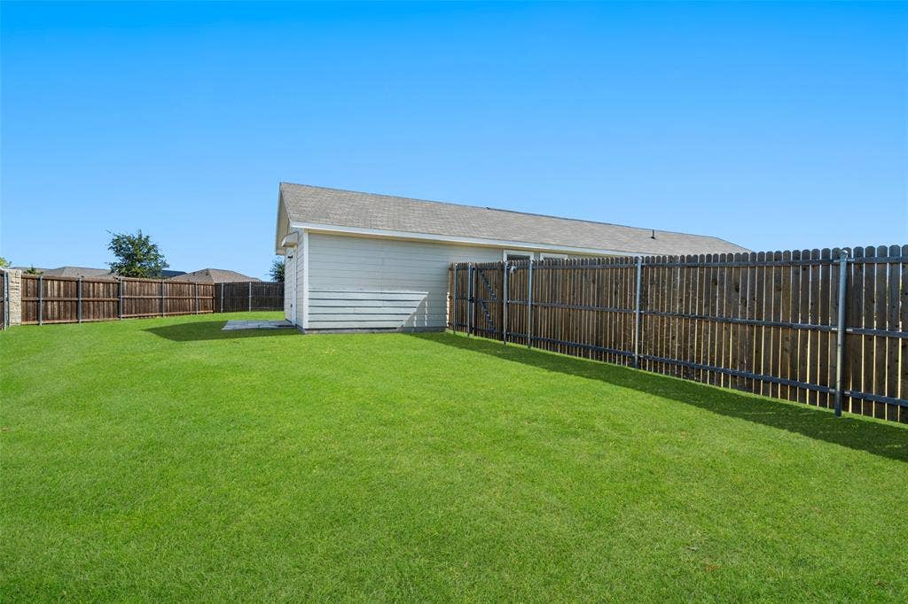 250 Herman Lane, Princeton, TX 75407 Expansive lawn area, full wood privacy fencing, concrete patio, and a detached structure with siding and a shingled roof