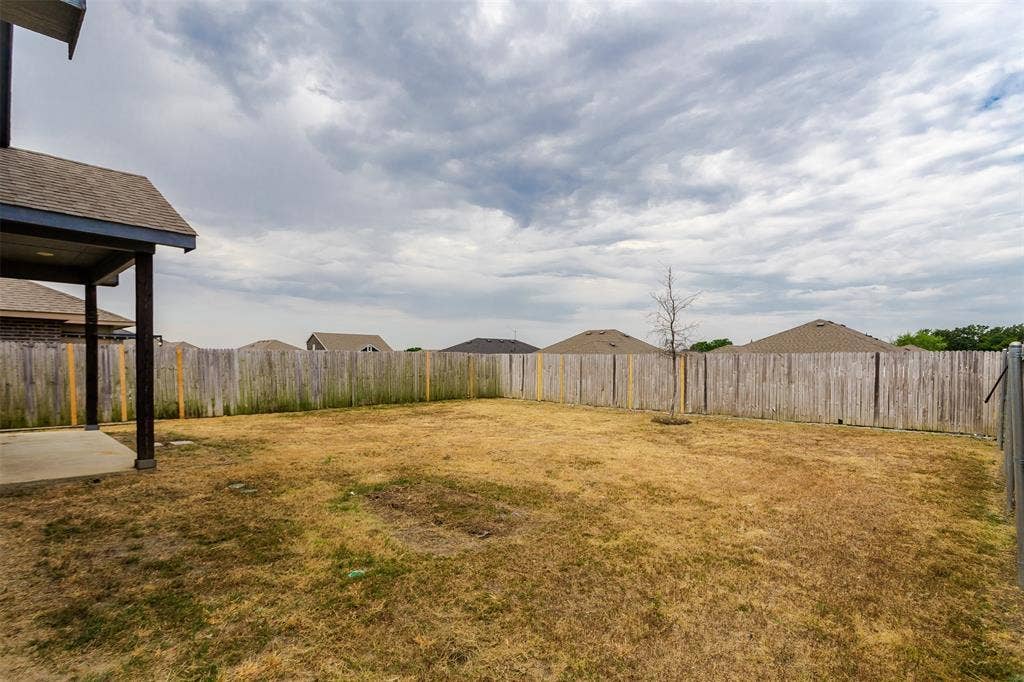 Backyard with a wood privacy fence, concrete patio, and a covered patio area with dark support posts