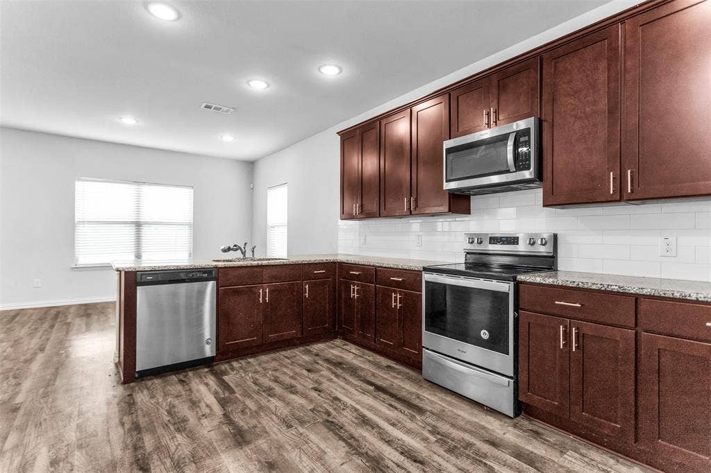 Kitchen featuring wood-finish flooring, dark wood cabinetry, stainless steel appliances, granite-style countertops, and a white subway tile backsplash