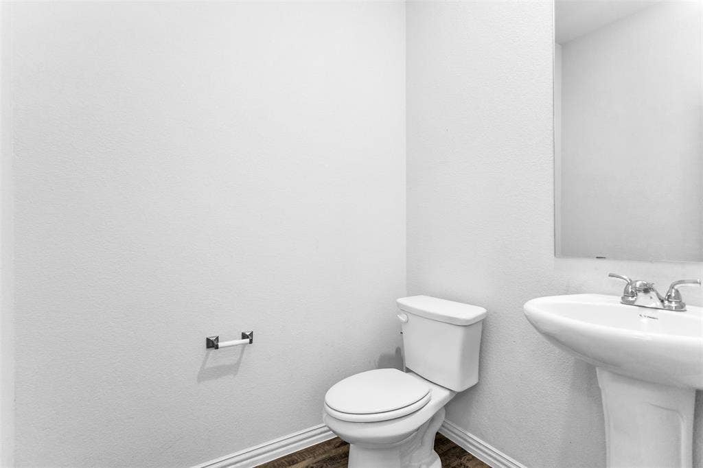 Pedestal sink with chrome faucet, wall-mounted mirror, and wood-finish flooring