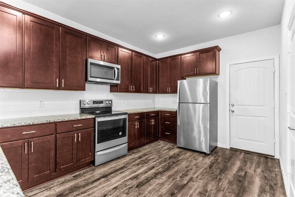 Kitchen featuring dark wood cabinetry, stainless steel appliances, a white subway tile backsplash, light-toned countertops, and wood-finish flooring