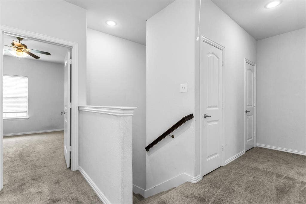 Carpeted hallway with white interior doors, a dark wood handrail, and an overhead recessed light