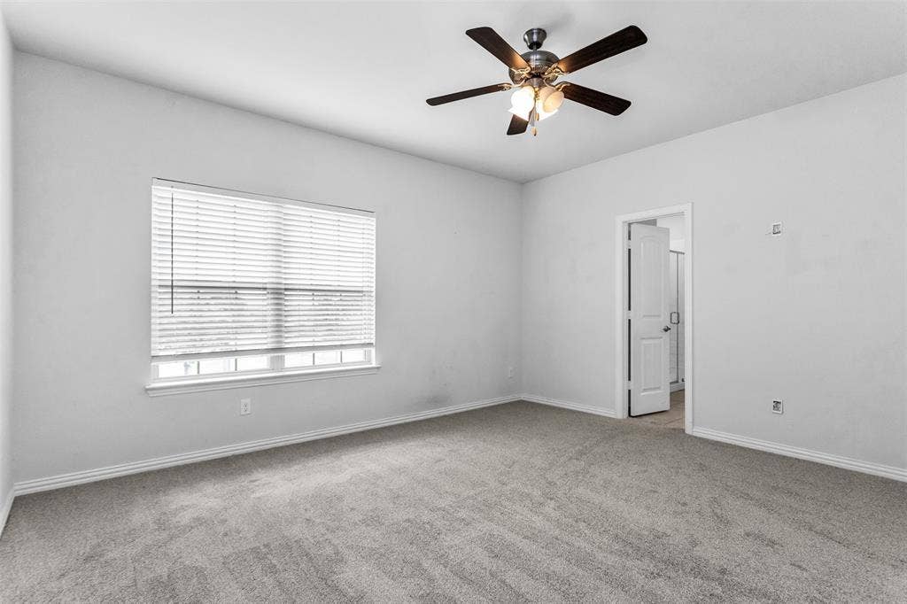 Wall-to-wall carpeting, window with horizontal blinds, ceiling fan with integrated lighting, and a white paneled door