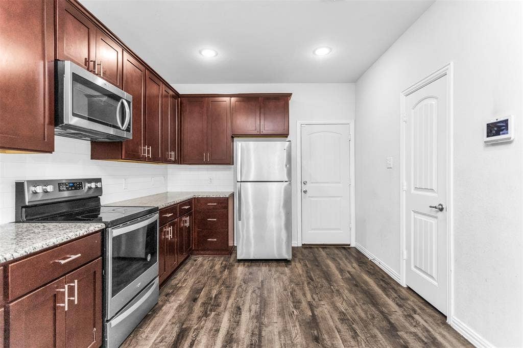 Kitchen featuring wood-finish cabinetry, stainless steel appliances, speckled countertops, white subway tile backsplash, and wood-finish flooring