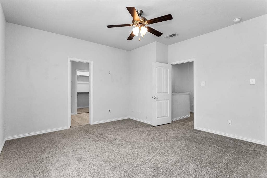 Spacious room featuring neutral carpet, light gray walls, a ceiling fan with integrated lighting, and white paneled doors
