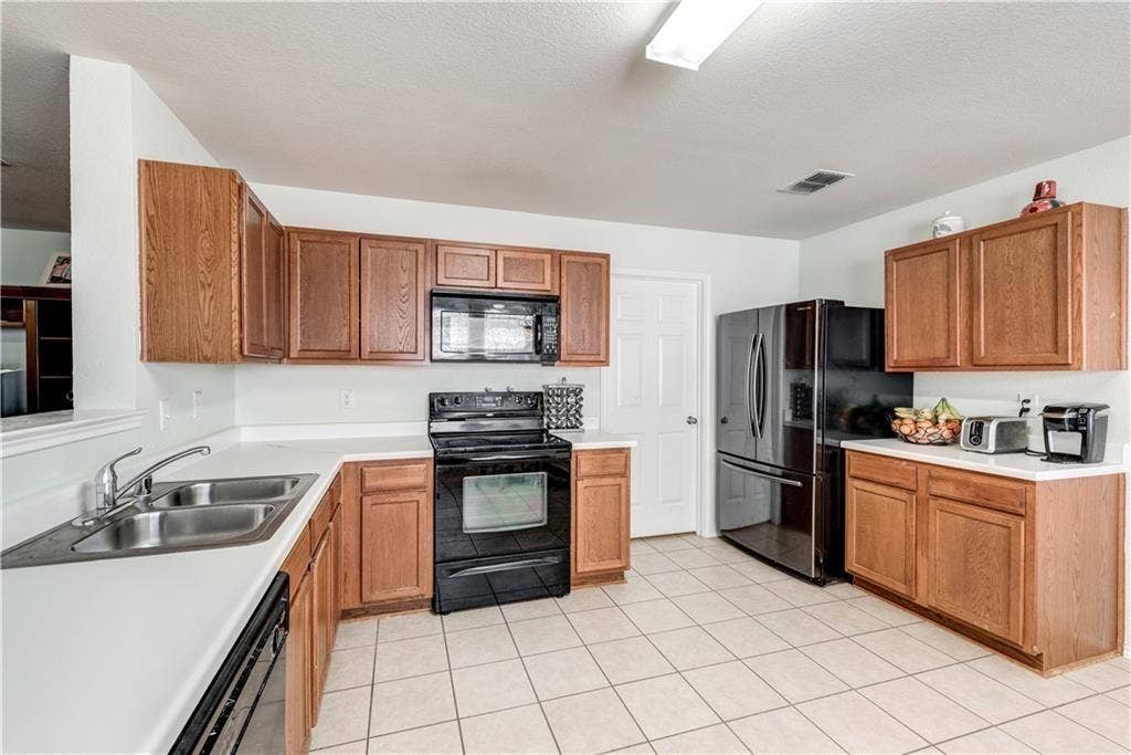12829 Pricklybranch Drive, Fort Worth, TX 76244 Kitchen featuring wood cabinetry, white countertops, stainless steel double basin sink, black appliances, and tile flooring