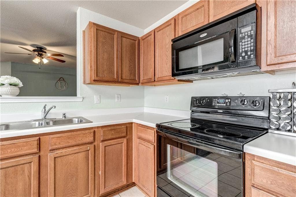 12829 Pricklybranch Drive, Fort Worth, TX 76244 Kitchen featuring wood-finish cabinetry, white countertops, a double basin stainless steel sink, and a black electric range with an overhead microwave