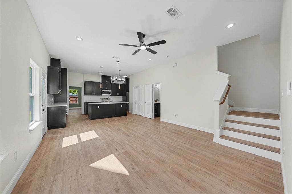 817 Stamps Avenue, Fort Worth, TX 76114 Open-concept living space featuring wood-finish flooring, a modern kitchen with dark cabinetry, stainless steel appliances, a kitchen island, and a staircase with a wood handrail