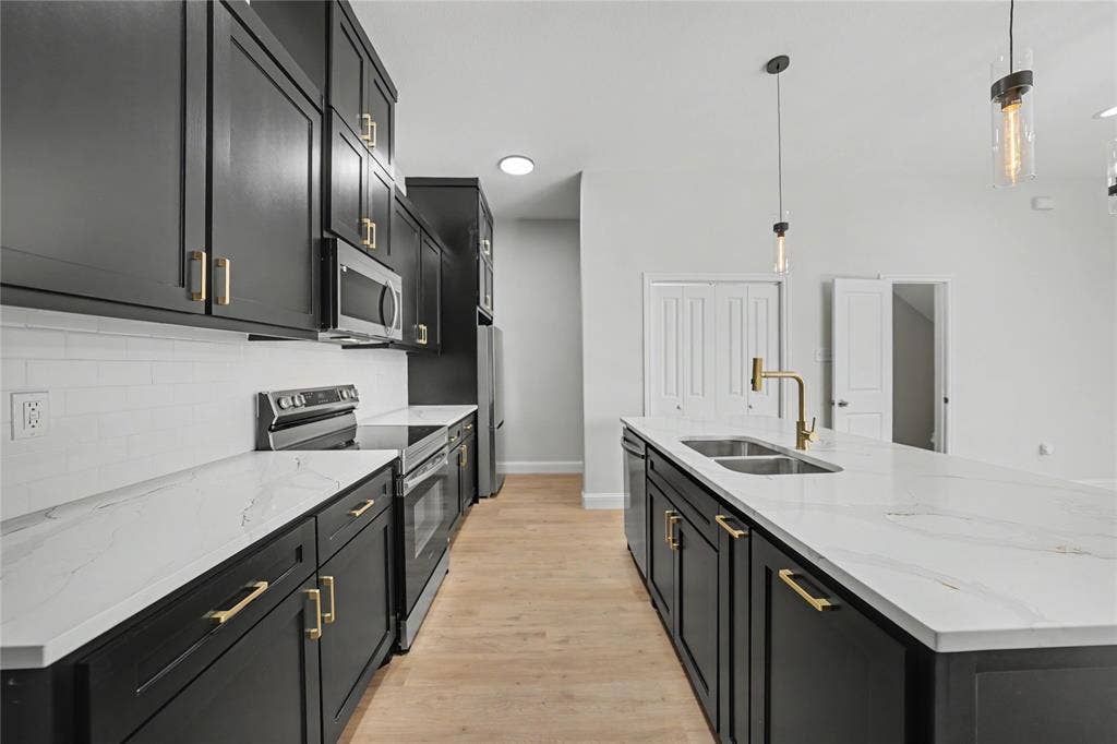 817 Stamps Avenue, Fort Worth, TX 76114 Kitchen featuring black cabinetry, stainless steel appliances, white subway tile backsplash, white countertops, and wood-finish flooring